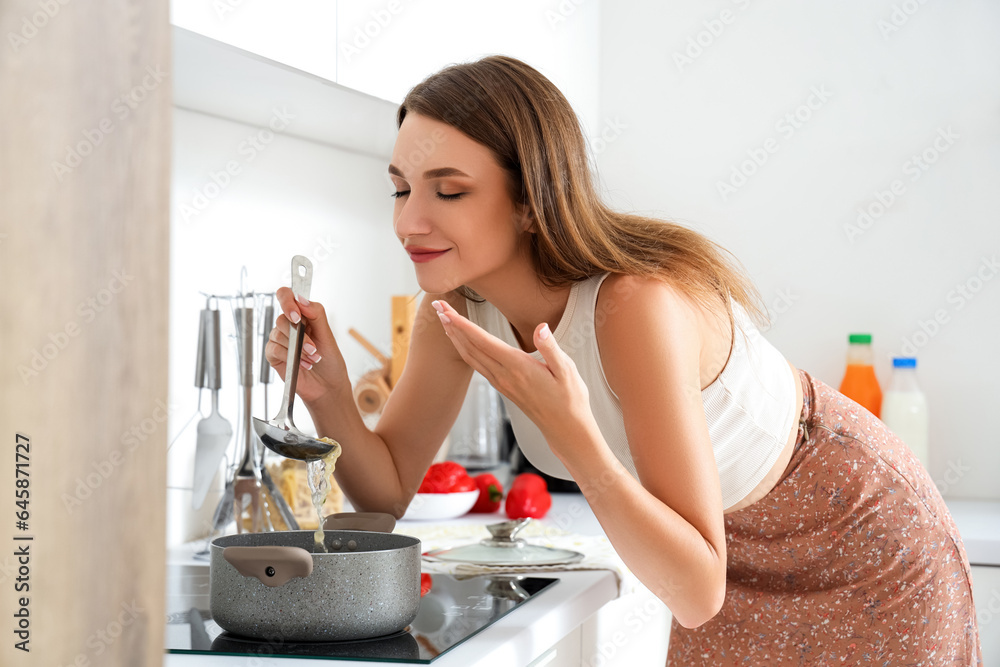 Young woman cooking chicken soup on stove in kitchen