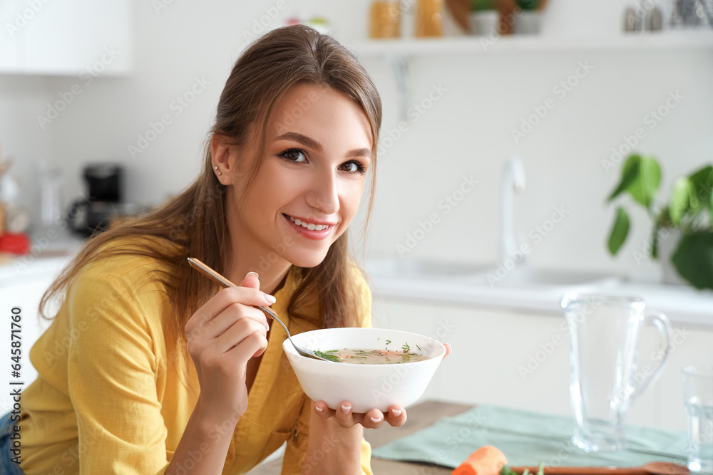 Young woman with bowl of chicken soup in kitchen, closeup