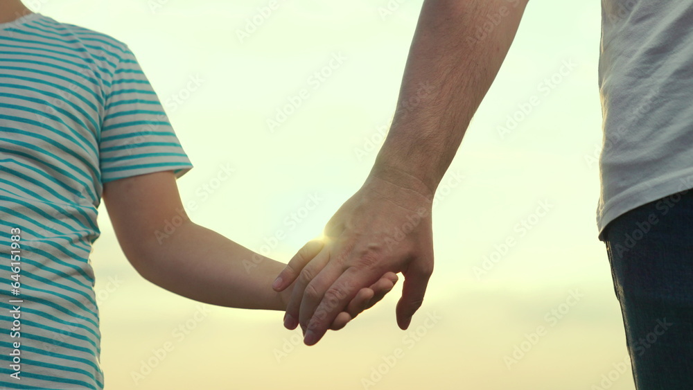 Adoption of child. Child son and dad hold hands close-up in nature in sun. Happy family, teamwork. C