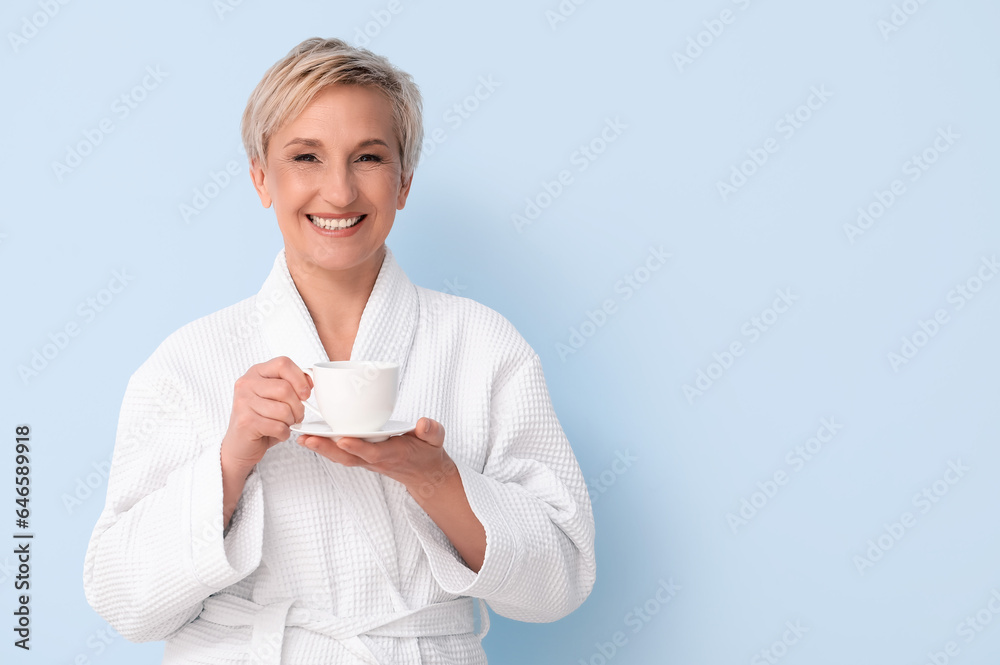 Mature woman in bathrobe with cup of coffee on blue background