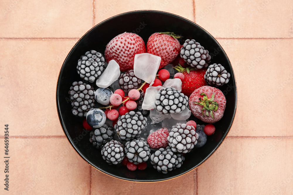 Bowl of frozen berries with ice on color tile background