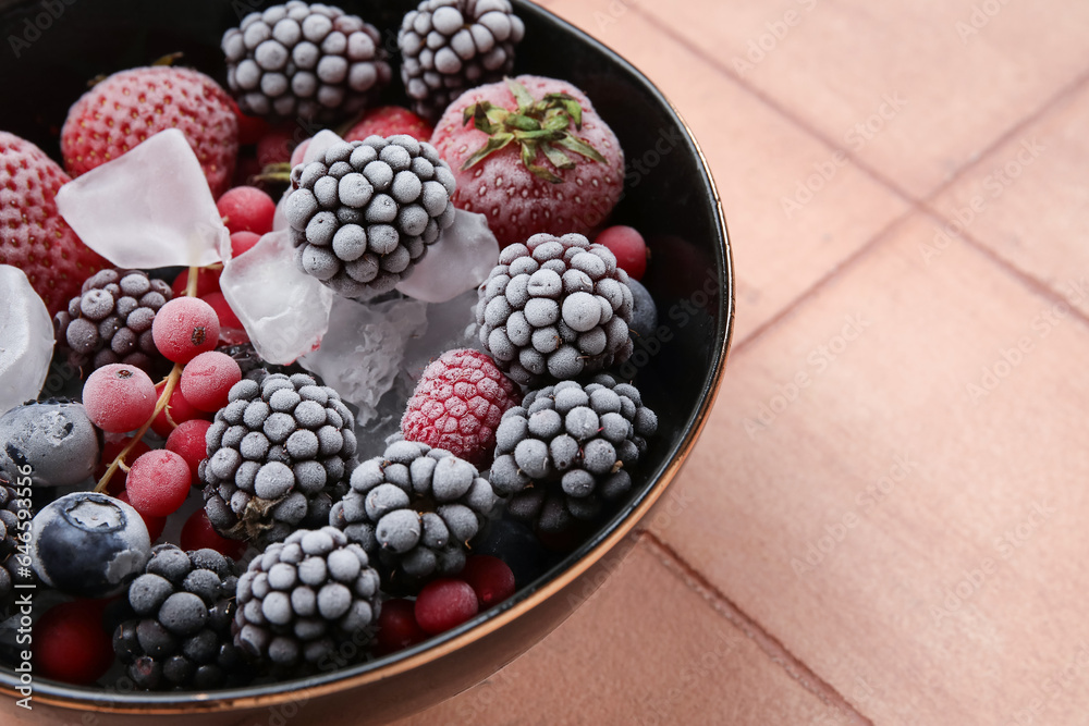 Bowl of frozen berries with ice on color tile background, closeup