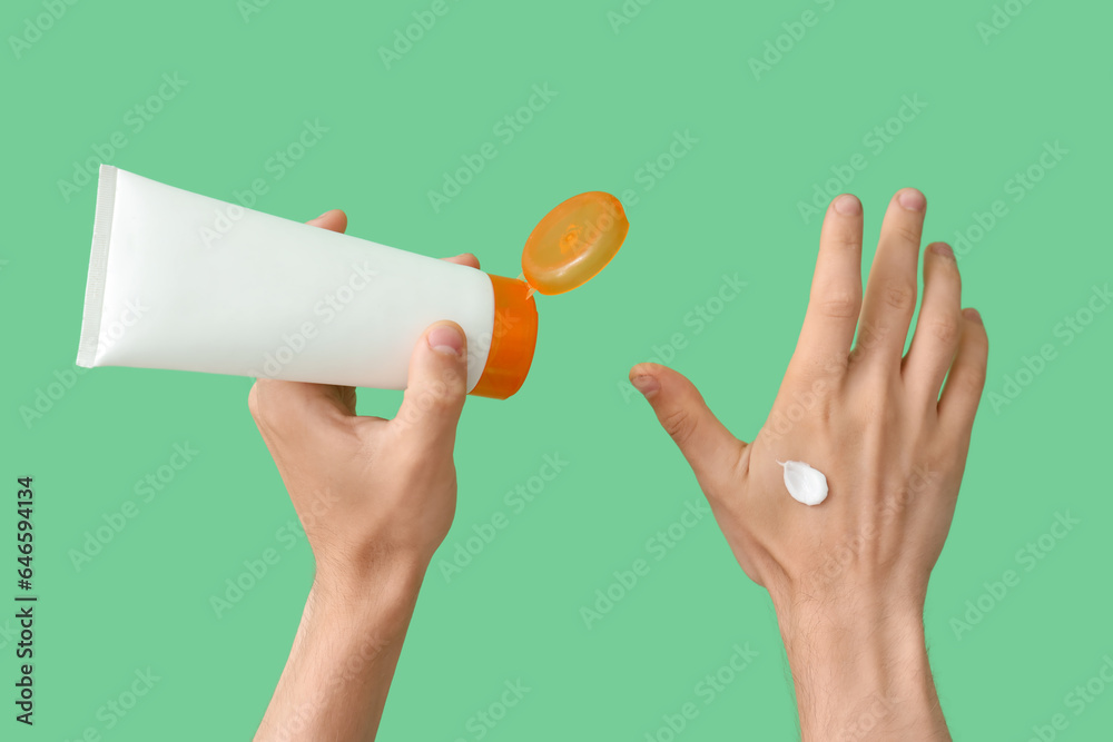 Female hands with bottle of sunscreen cream on green background