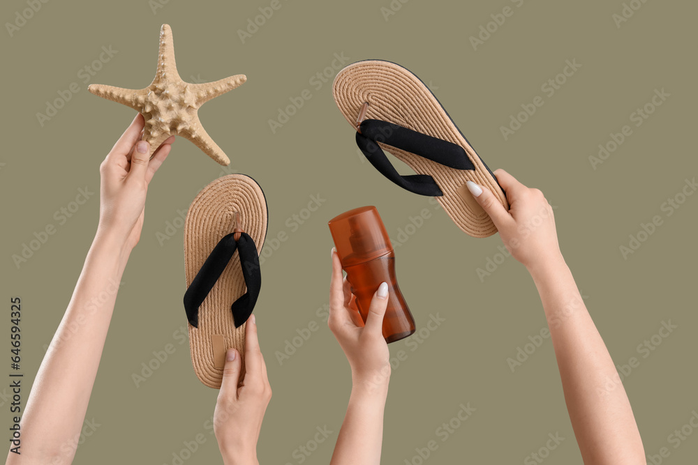 Female hands with bottle of sunscreen cream, flip flops and starfish on green background