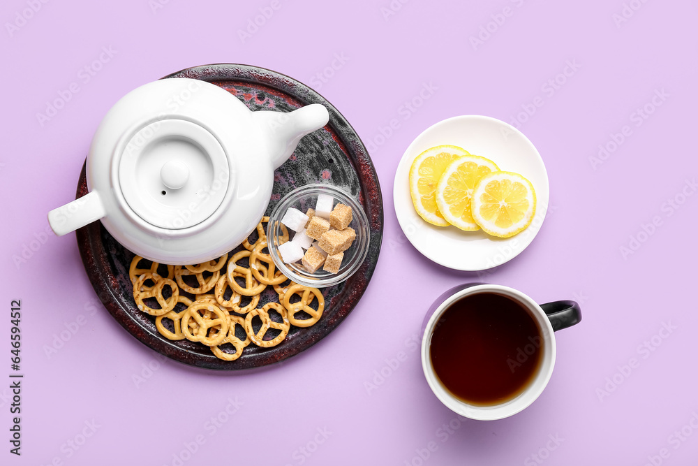 Teapot, cup of tea, lemon slices and pretzels on color background