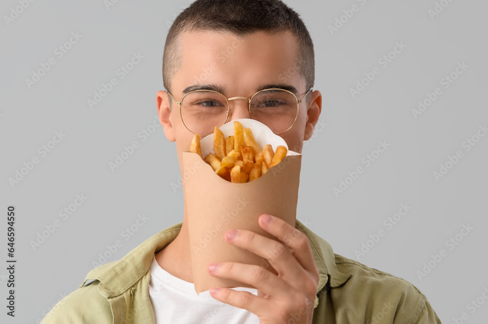 Young man with french fries on light background, closeup