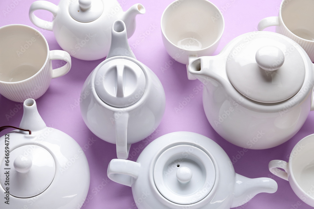 Many porcelain teapots and cups on lilac background