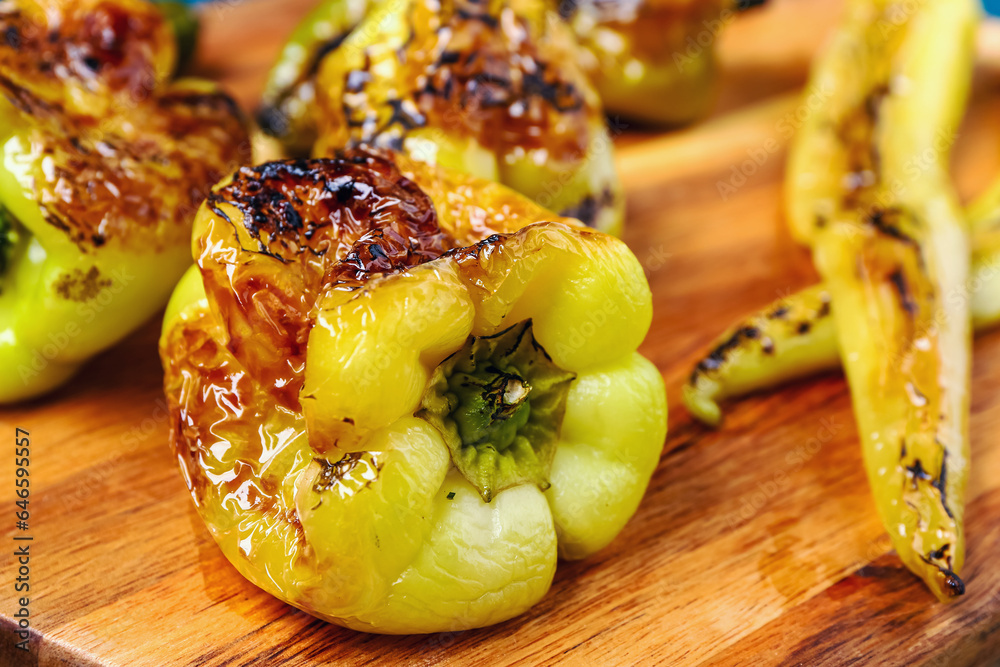 Wooden board with different grilled peppers, closeup