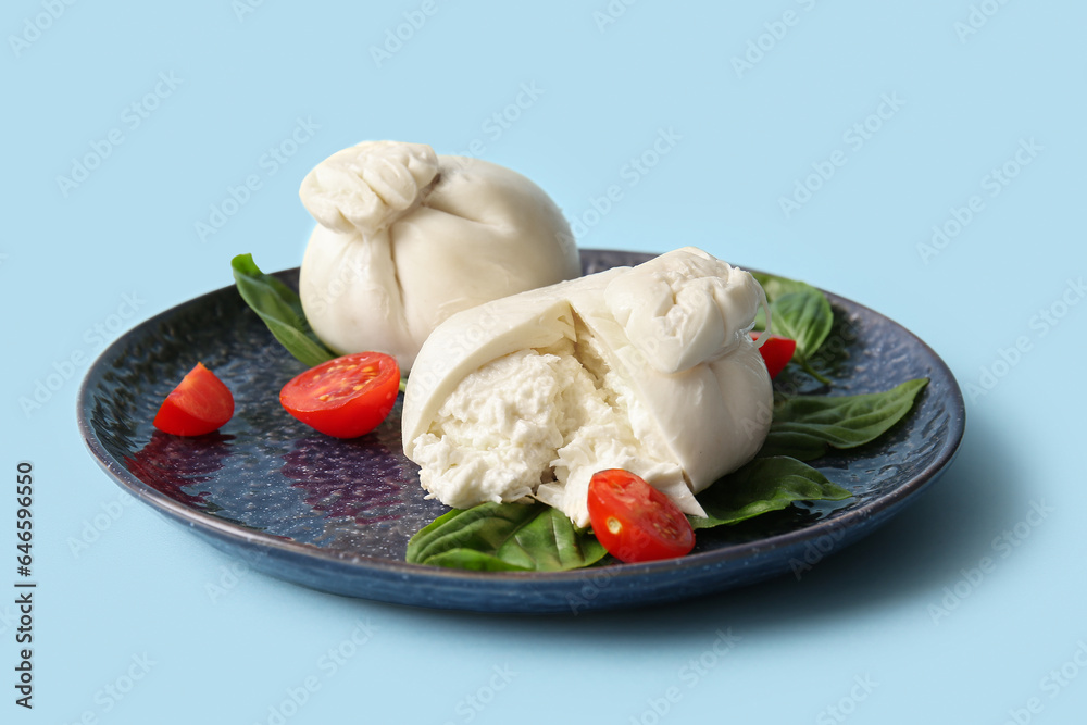 Plate of tasty Burrata cheese with basil and tomatoes on blue background