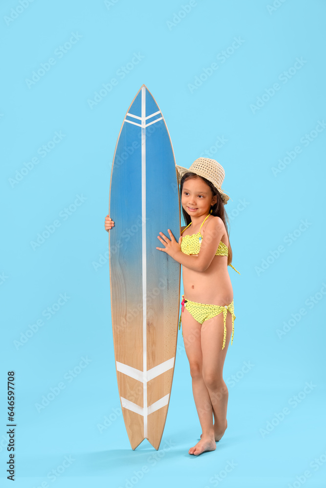 Little Asian girl with surfboard on blue background