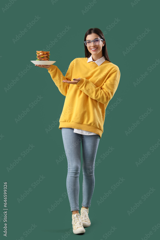 Young woman with big sandwich on green background