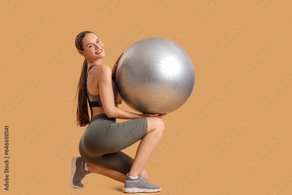 Sporty young woman with fitball on beige background