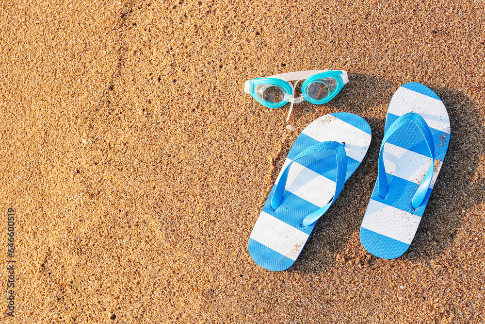 Stylish flips flops with goggles on sand at resort