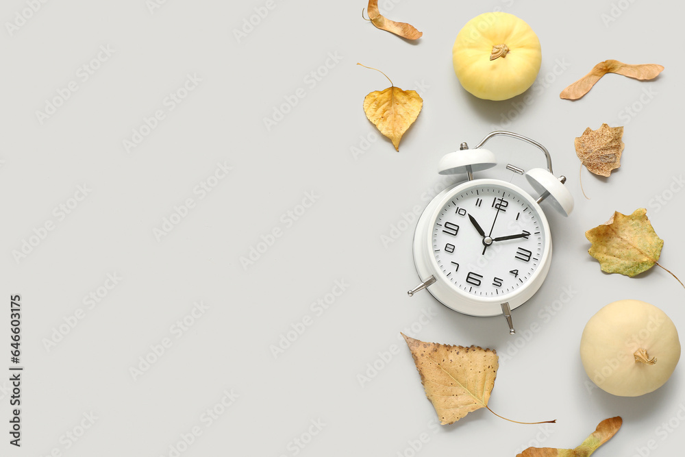 Alarm clock with fallen leaves and pumpkins on light background