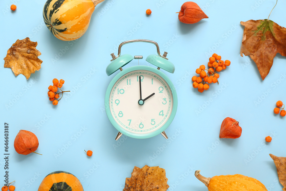 Alarm clock with fallen leaves and berries on blue background