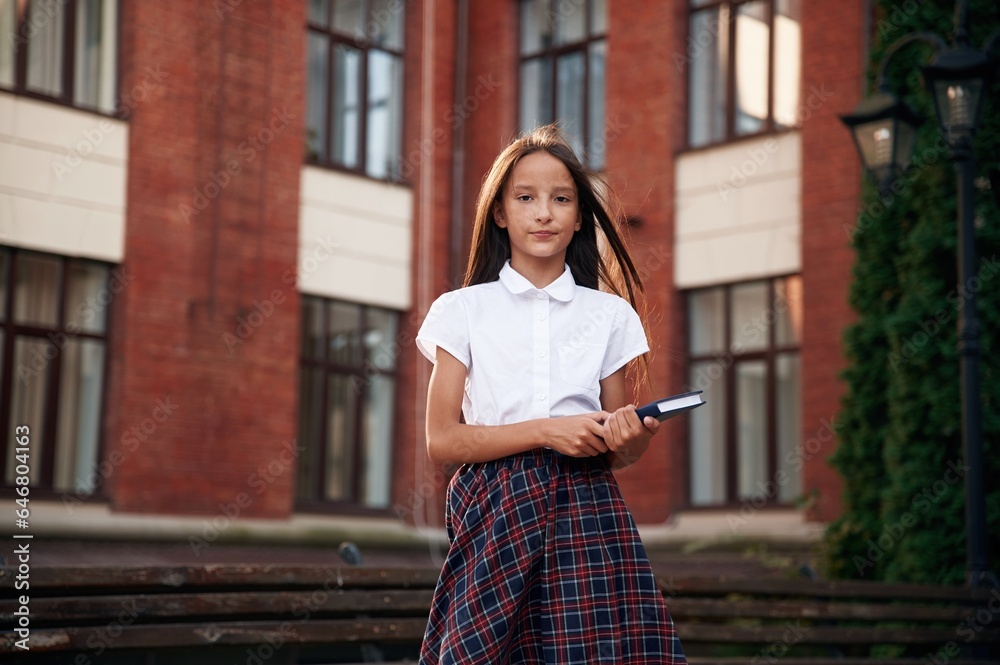 Orange colored building. School girl in uniform is outdoors