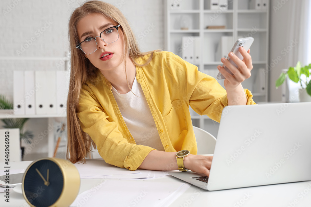 Young businesswoman working with mobile phone and laptop under deadline in office