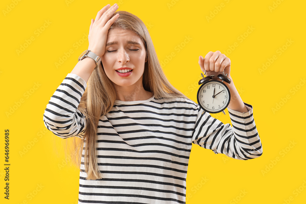 Stressed young woman with alarm clock on yellow background. Deadline concept