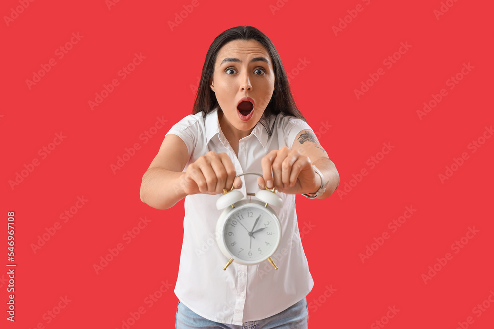 Shocked young woman with alarm clock on red background. Deadline concept