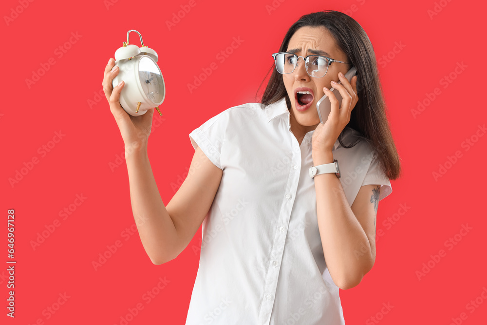 Stressed young woman with alarm clock on red background. Deadline concept