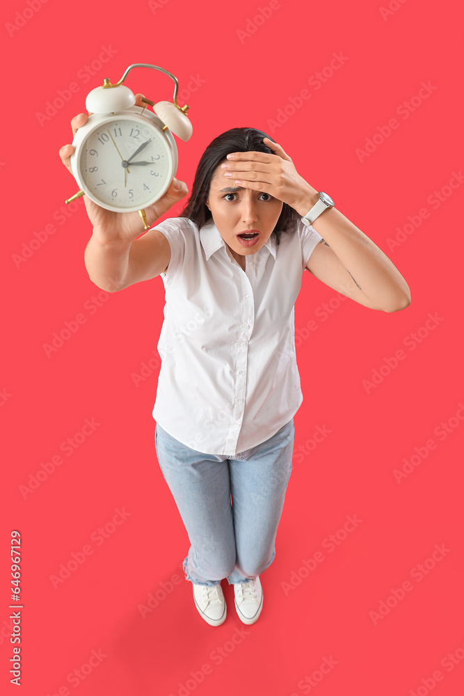 Stressed young woman with alarm clock on red background. Deadline concept