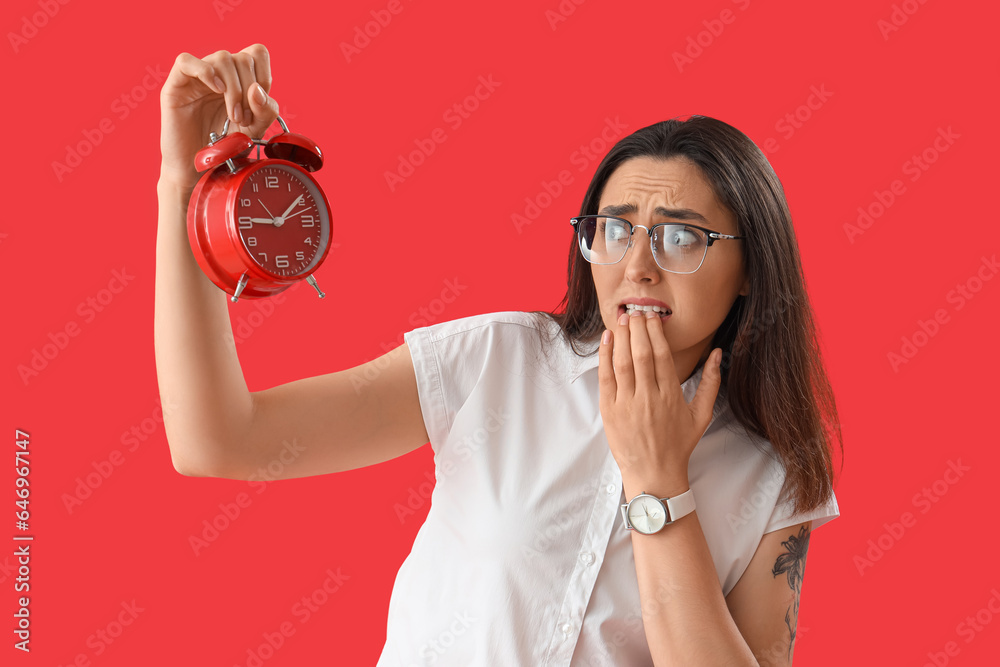 Worried young woman with alarm clock on red background. Deadline concept