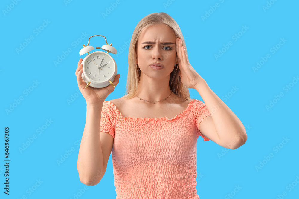 Stressed young woman with alarm clock on blue background. Deadline concept