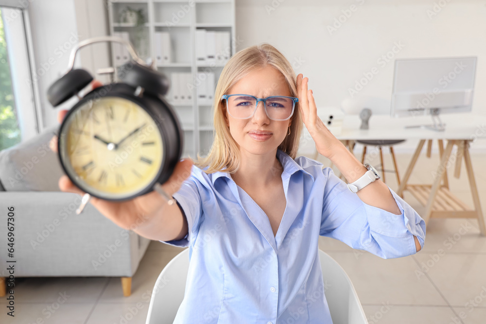 Stressed young businesswoman with alarm clock working under deadline in office, closeup