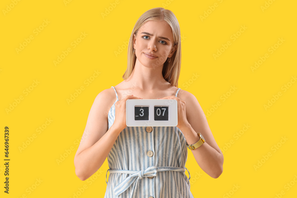 Stressed young woman with clock on yellow background. Deadline concept