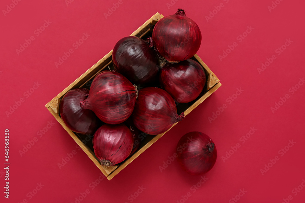 Wooden box with fresh red onions on color background