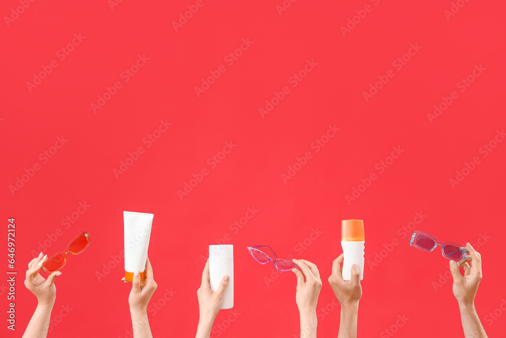 Female hands with bottles of sunscreen cream and sunglasses on red background