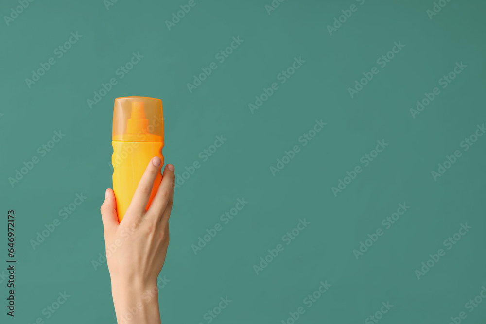 Female hand with bottle of sunscreen cream on green background