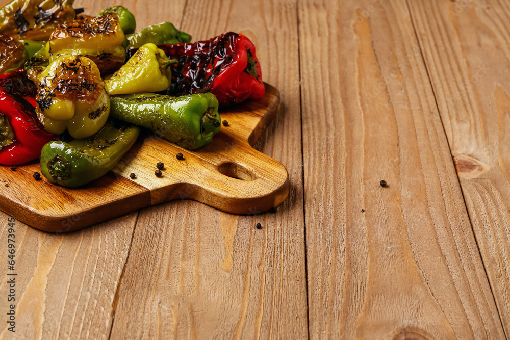 Board with different grilled peppers on wooden background