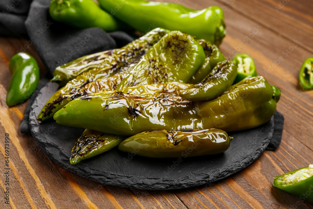 Slate board with grilled chili peppers on wooden background