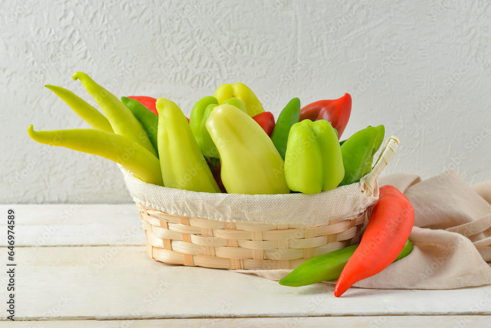 Wicker basket with different fresh peppers on white wooden table