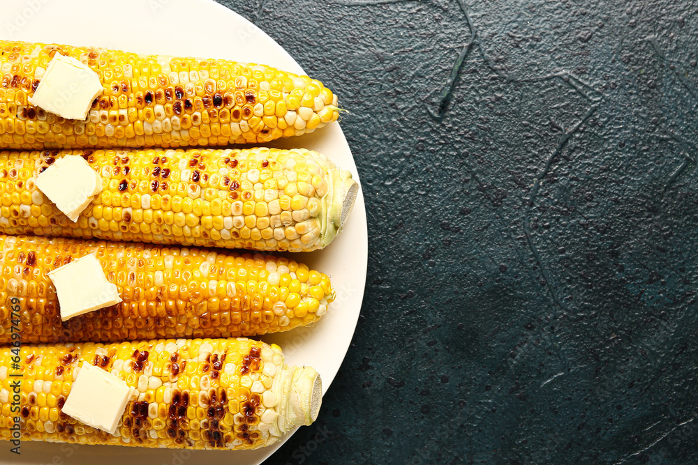 Plate of tasty grilled corn cobs with butter on dark background