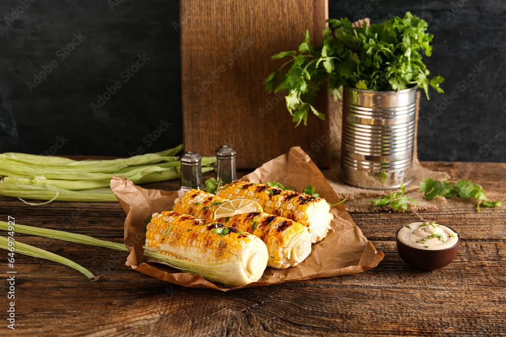 Baking paper with tasty grilled corn cobs and parsley on wooden table