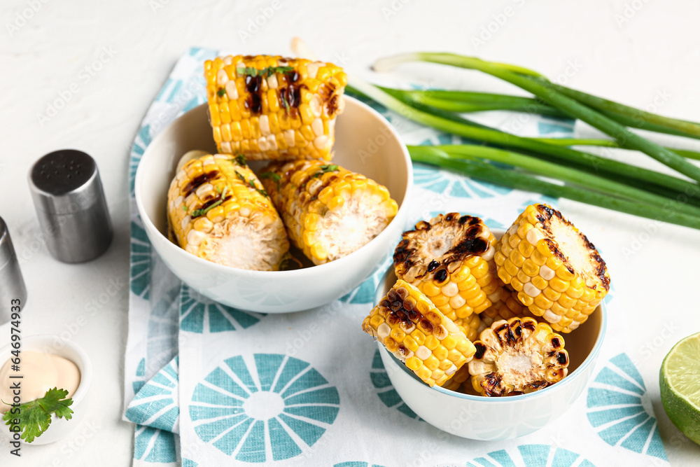 Bowls with tasty grilled corn cobs and green onion on white background