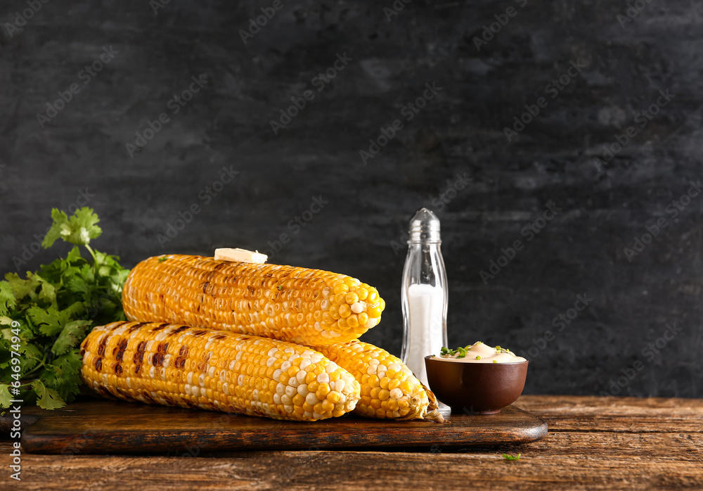 Board of tasty grilled corn cobs with butter and parsley on wooden table