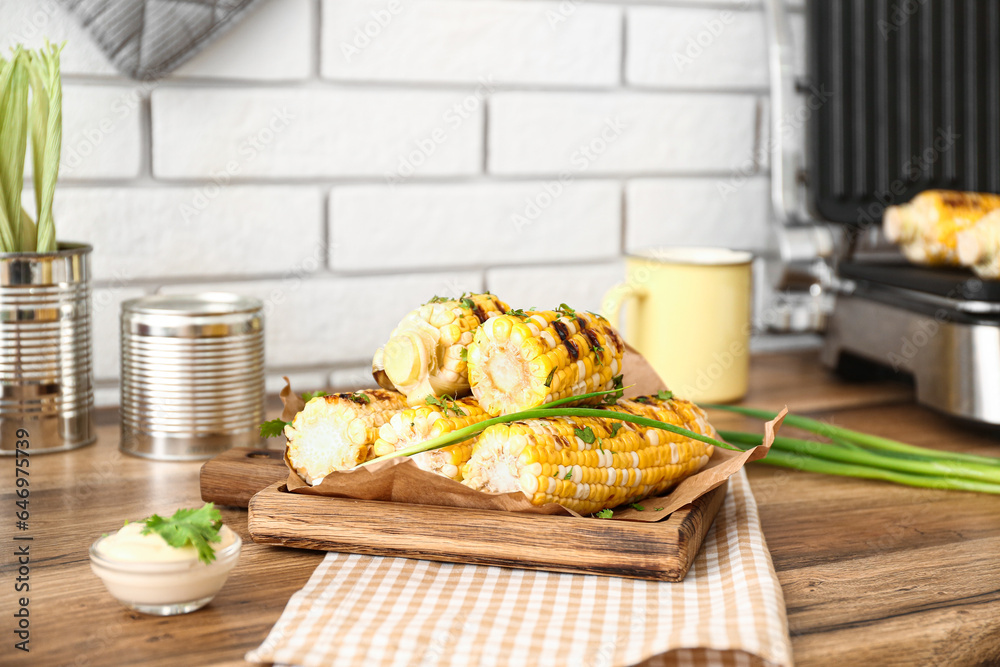 Board with tasty grilled corn on wooden kitchen counter