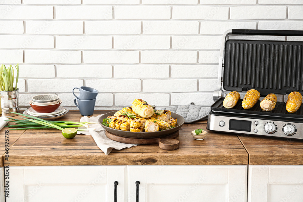 Plate and electric grill with tasty corn on wooden kitchen counter