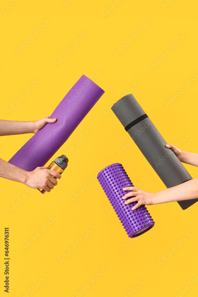 Hands holding yoga mats, bottle of water and massage roller on orange background