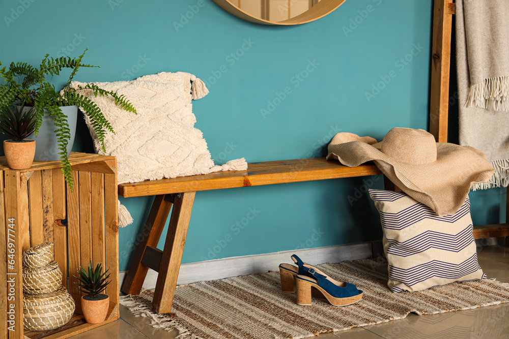 Wooden bench with pillows, female accessories and houseplants near blue wall in hall