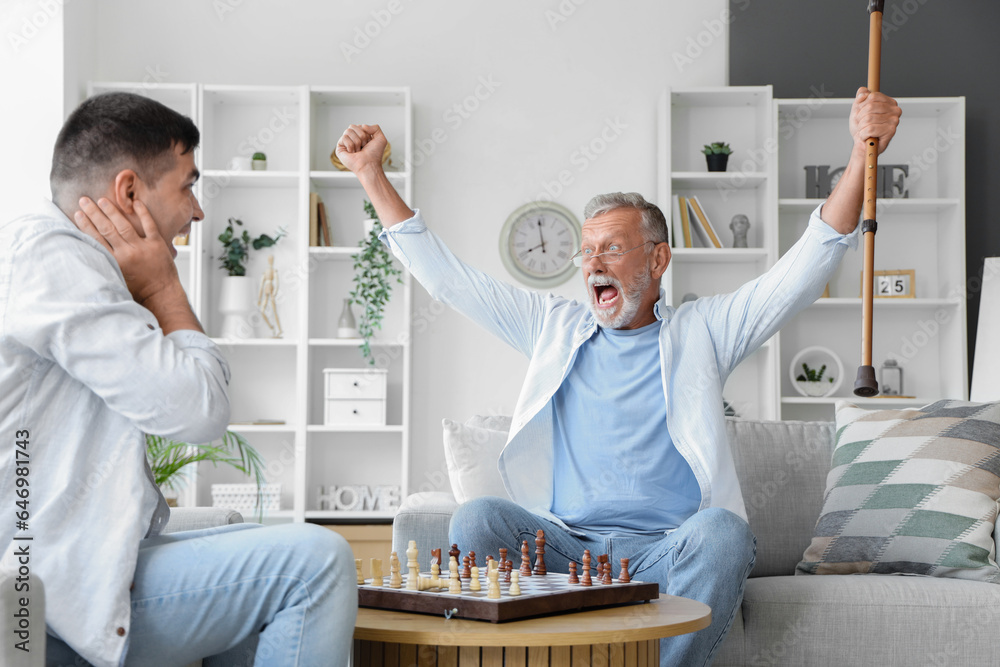 Happy senior man with his son playing chess at home