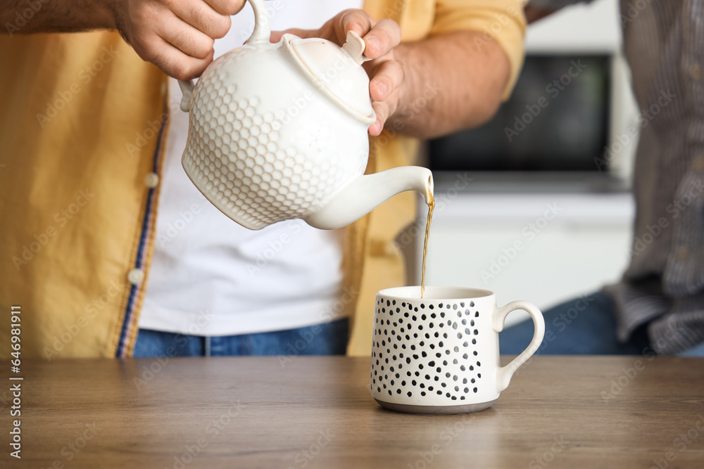 Young man pouring hot tea for his father in kitchen, closeup