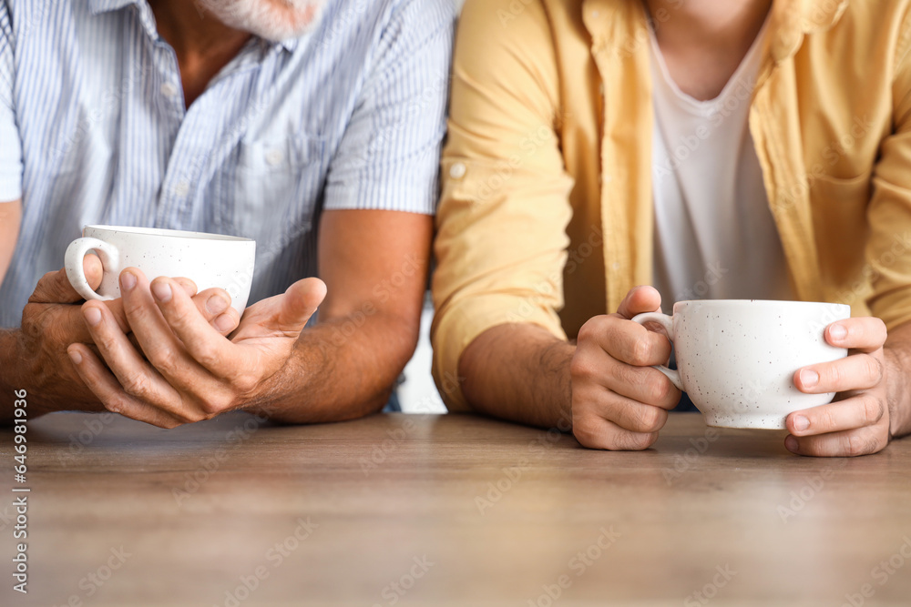 Senior man with his son drinking tea in kitchen, closeup