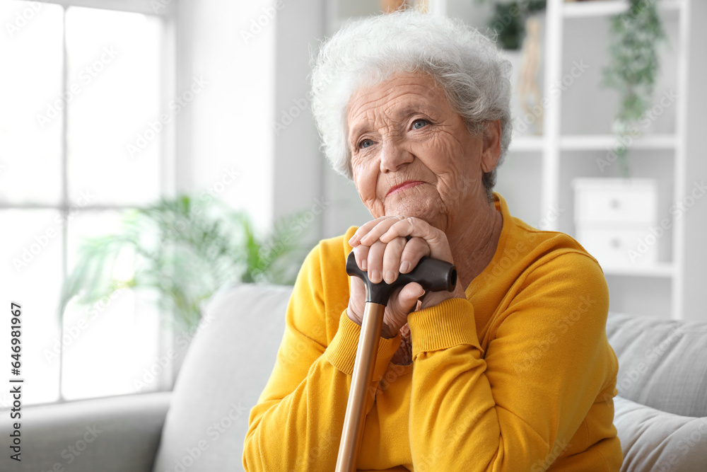 Senior woman with walking stick sitting on sofa at home