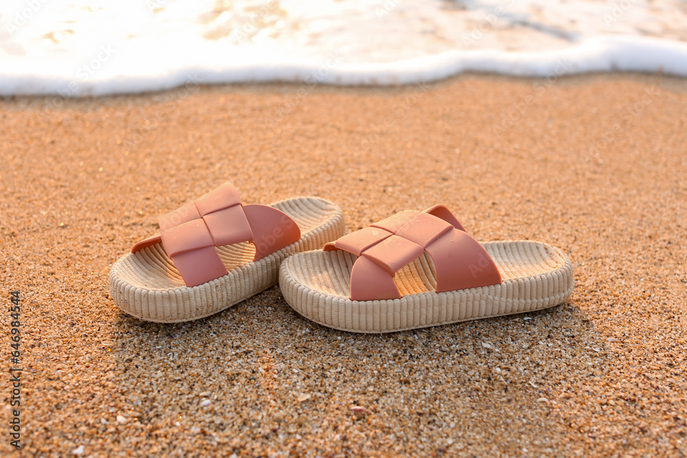 Stylish flips flops on sand near ocean at resort