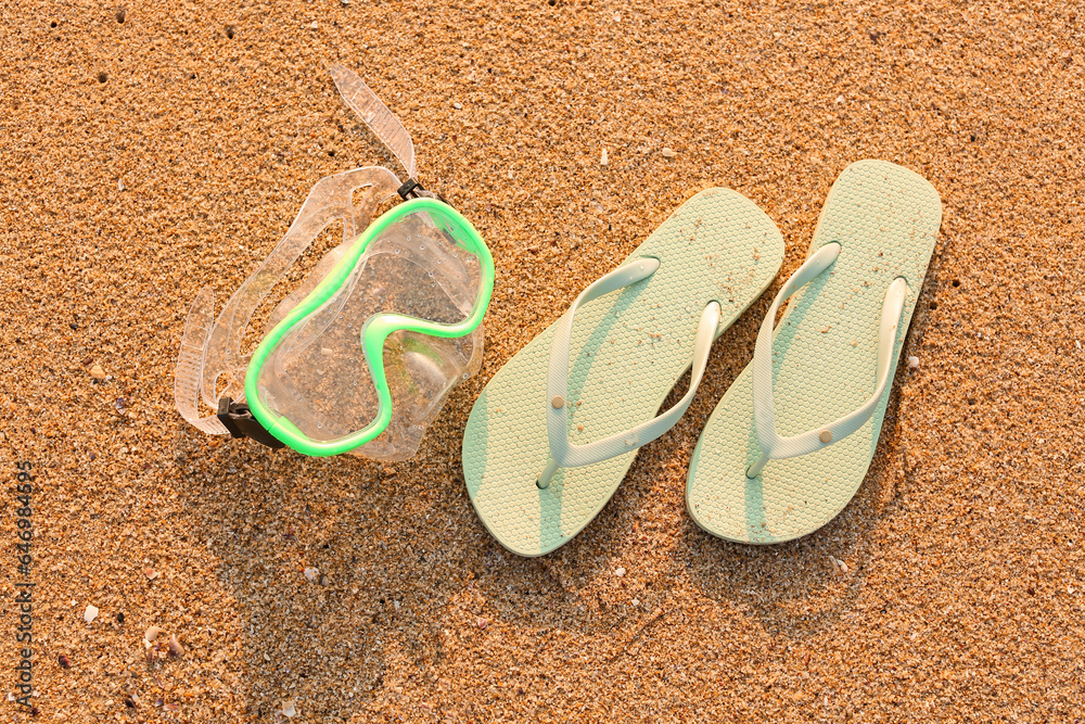 Stylish flips flops with snorkeling mask on sand at resort