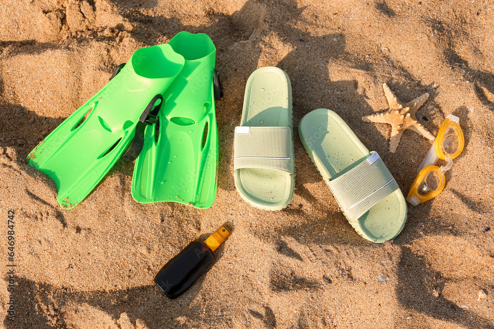 Stylish flips flops with flippers, goggles and sunscreen cream on sand at resort